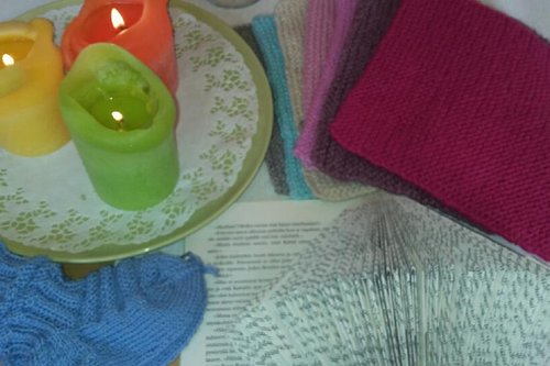 Erilaisia käsitöitä sekä keltainen, oranssi ja vaalean vihreä sytytetty kynttilä.